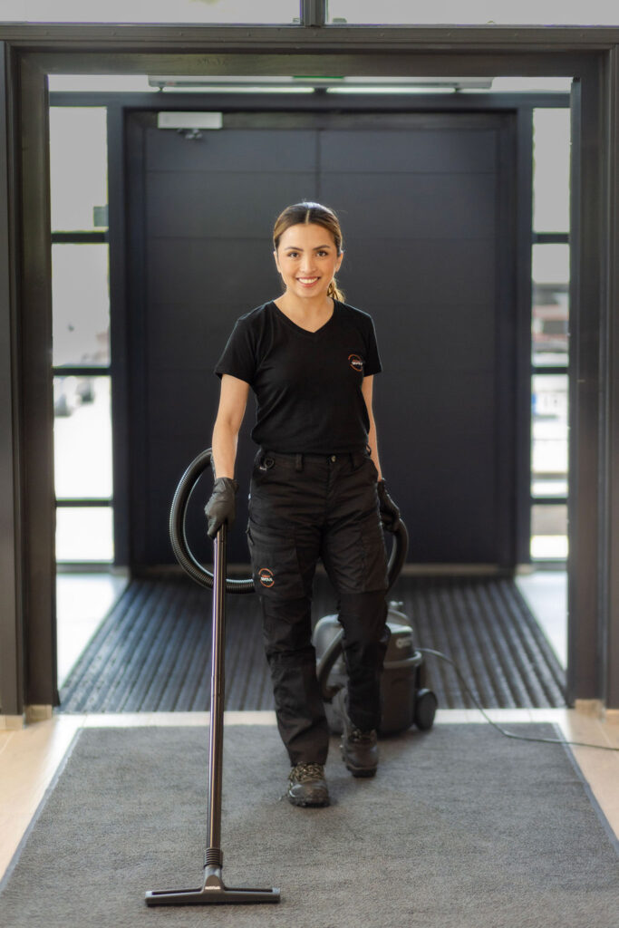 Siskon Siivous - siivoja imuroimassa toimiston eteisenmattoa.